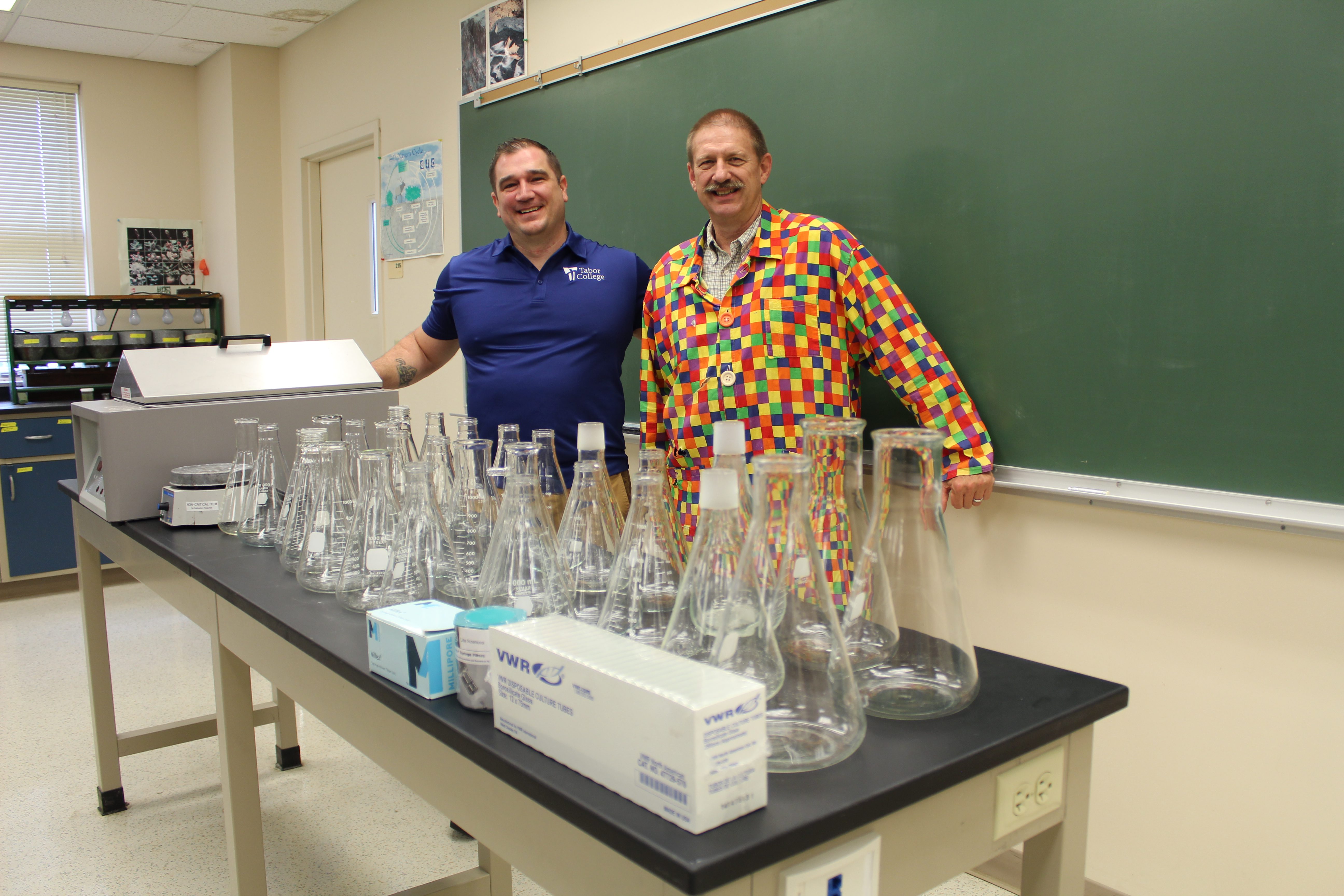 Professors Josh McLoud and Norman Schmidt stand in front of science equipment